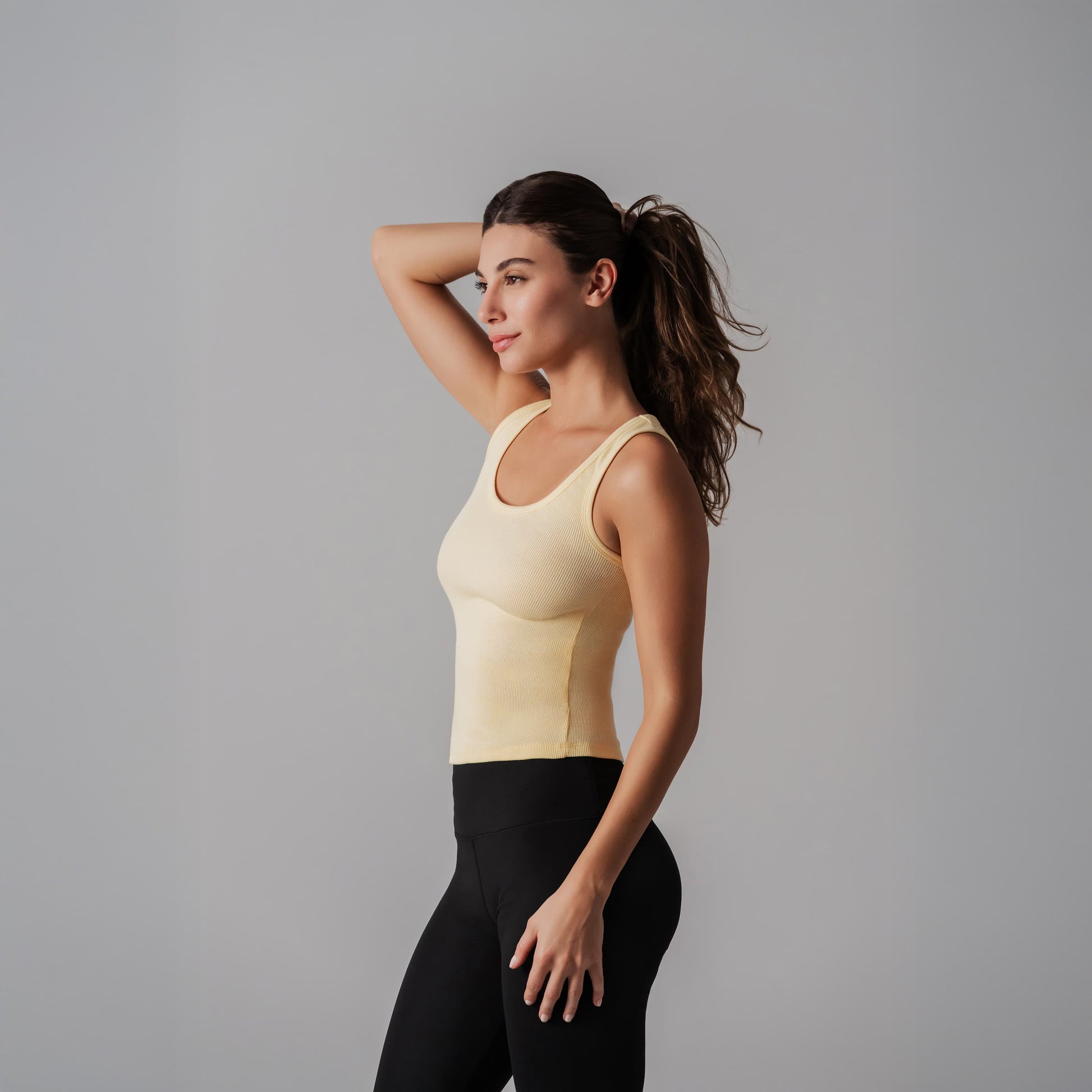 Woman wearing a yellow tank top and black leggings against a gray background