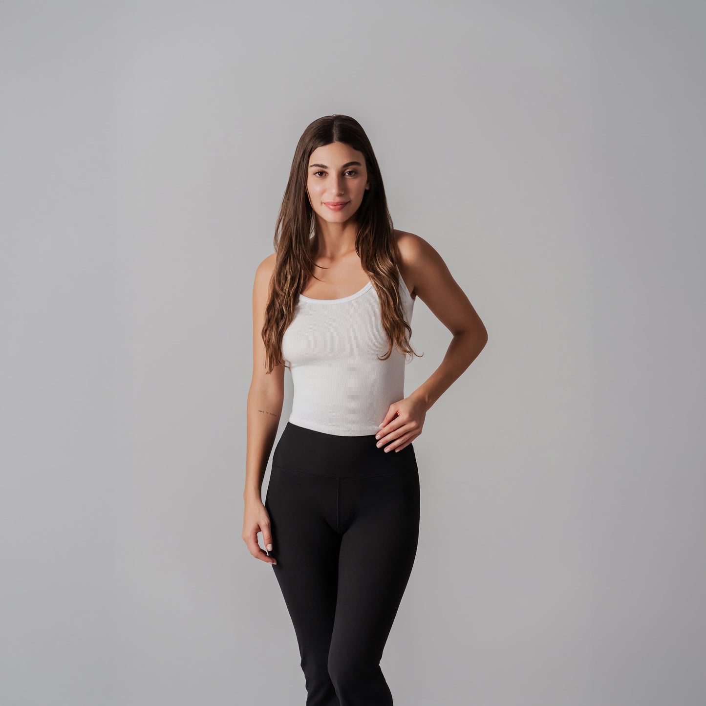Woman wearing a white tank top and black leggings against a gray background