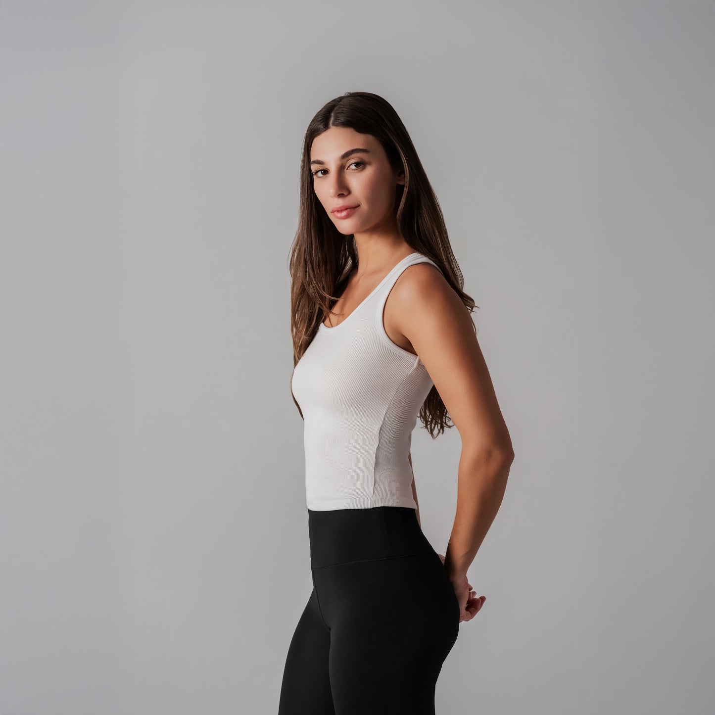 Woman wearing a white sleeveless top and black pants against a gray background
