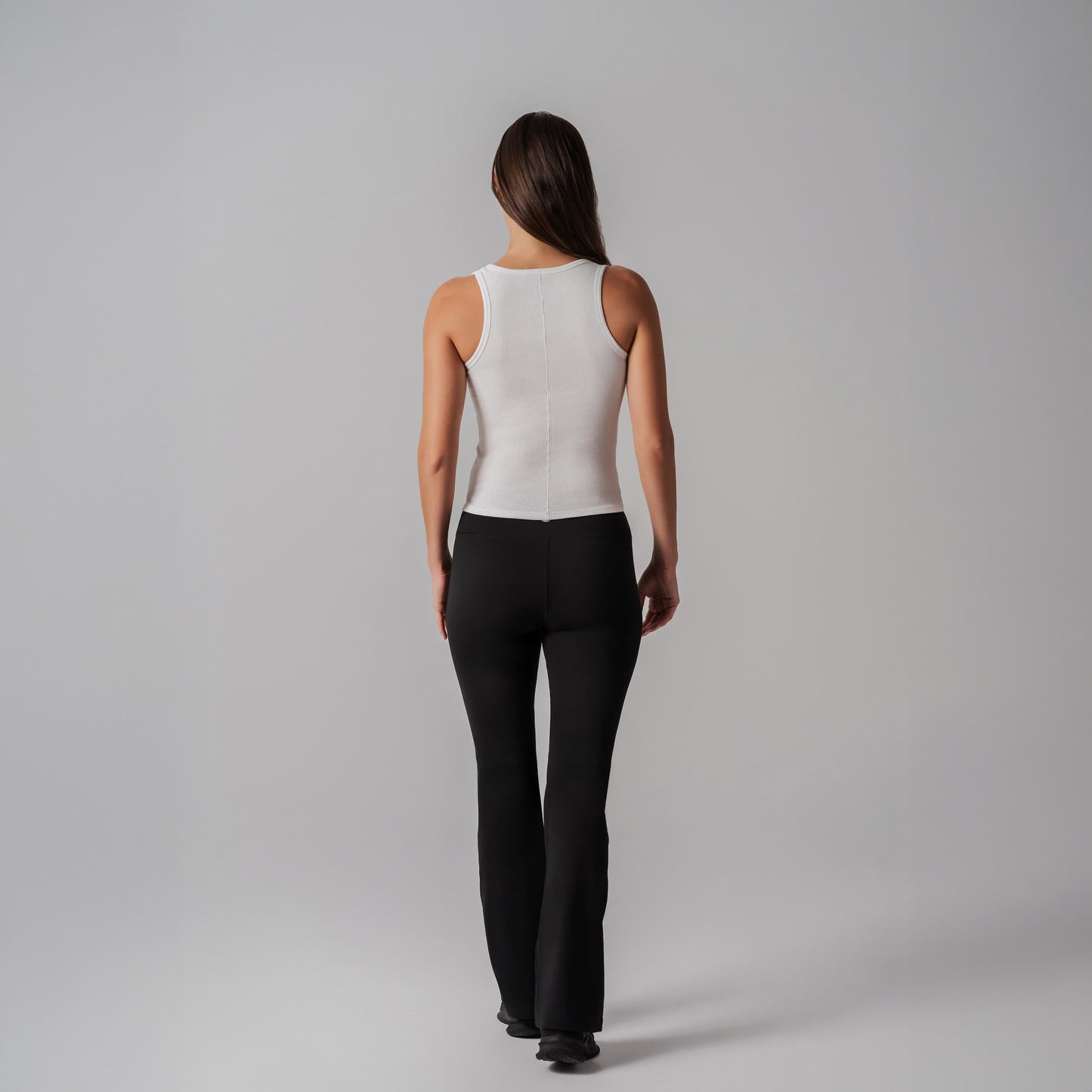 Person wearing a white sleeveless tank and black pants on a gray background