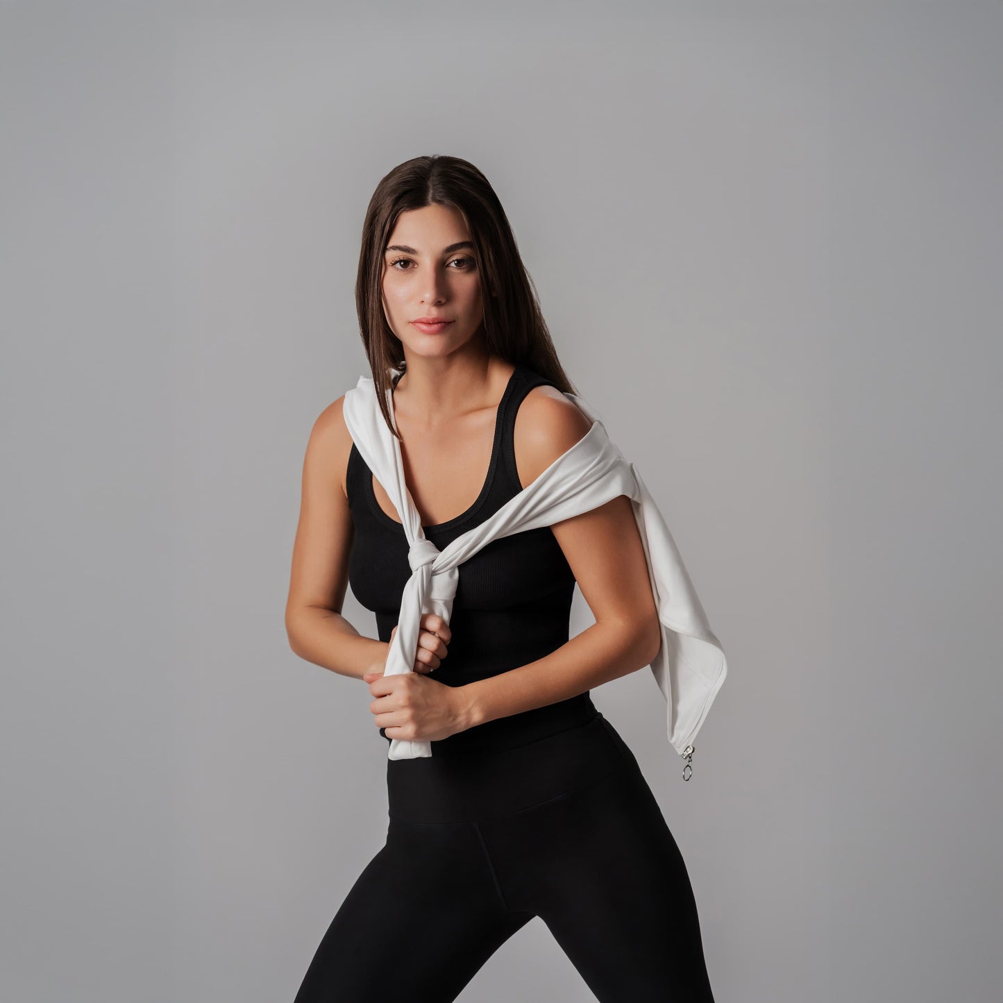 Woman in black athletic wear holding a white jacket against a gray background