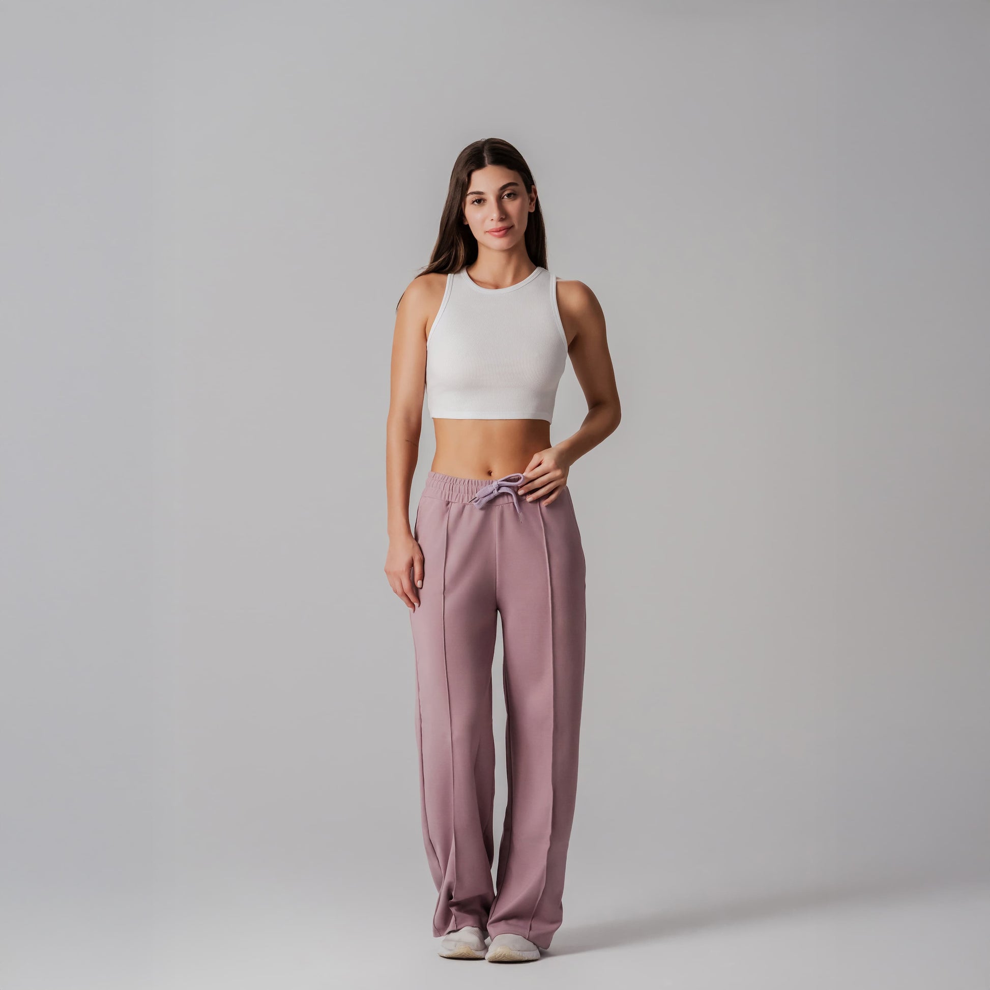 Woman wearing a white crop top and pink pants on a gray background