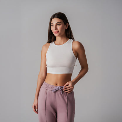 Woman wearing a white sports bra and pink pants against a gray background