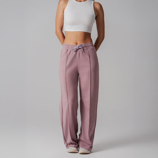 Person wearing pink sweatpants and a white crop top on a gray background