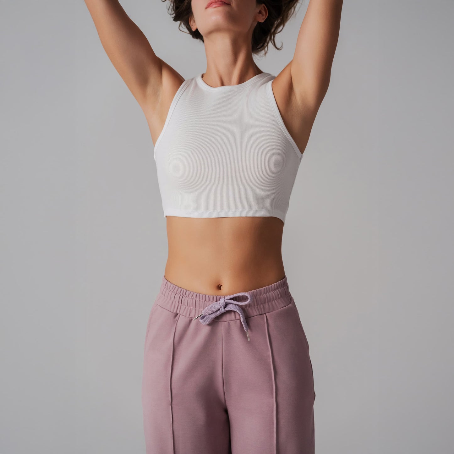 Person wearing a white crop top and pink pants against a gray background
