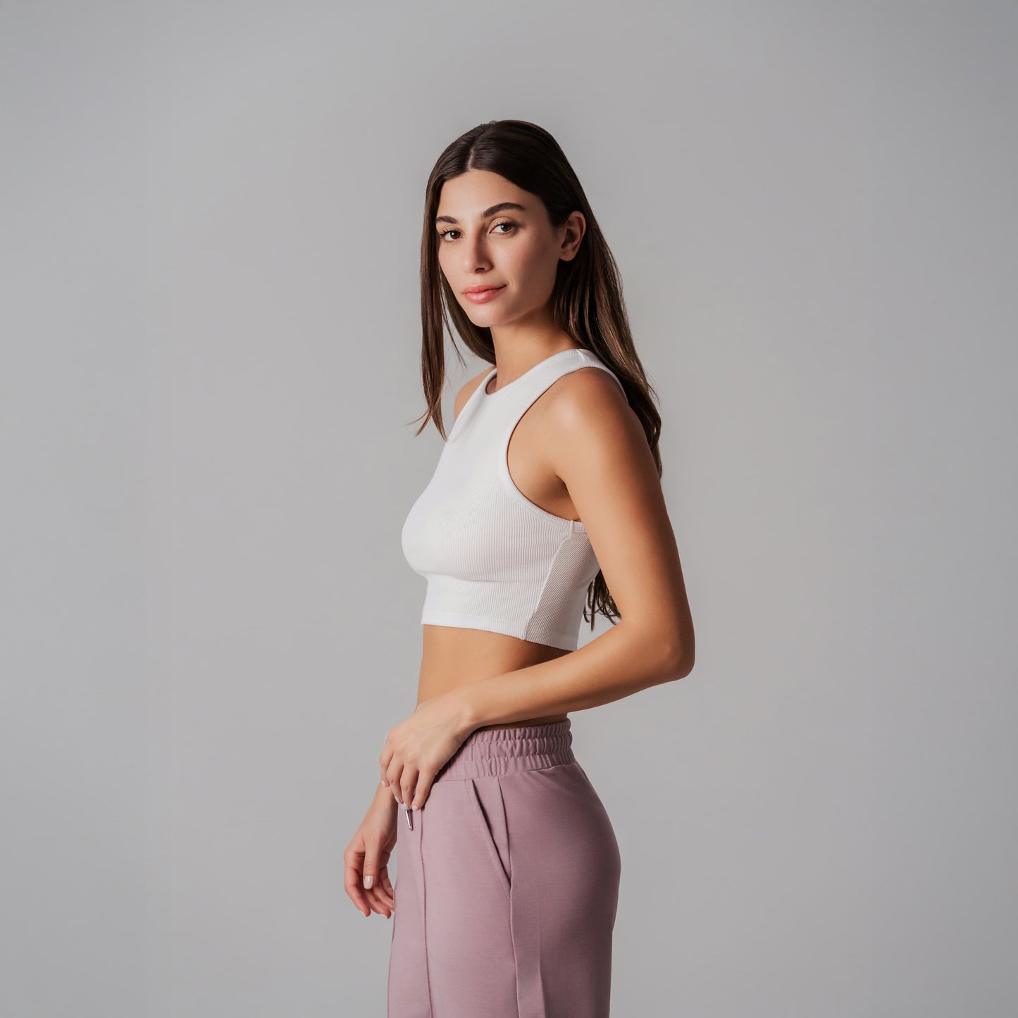 Woman wearing a white crop top and pink pants against a gray background