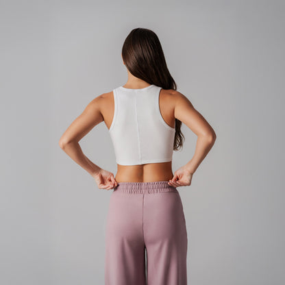 Woman wearing a white crop top and purple pants against a gray background
