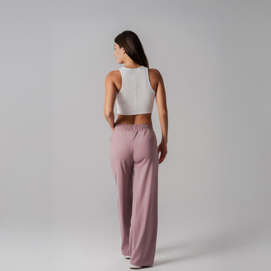 Woman wearing a white crop top and pink pants on a gray background