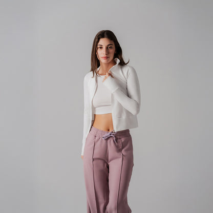 Woman wearing a white cropped jacket and pink pants against a gray background