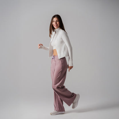 Woman wearing a white jacket and pink pants on a plain background