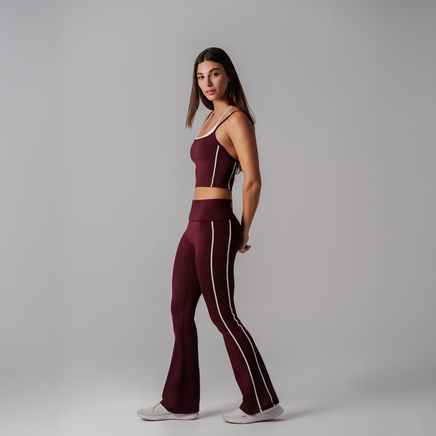 Woman wearing a burgundy athletic outfit with white stripes on a gray background