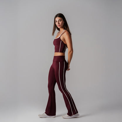 Woman wearing a burgundy athletic outfit with white stripes on a gray background