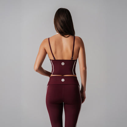Woman wearing a burgundy sports bra and leggings set on a gray background
