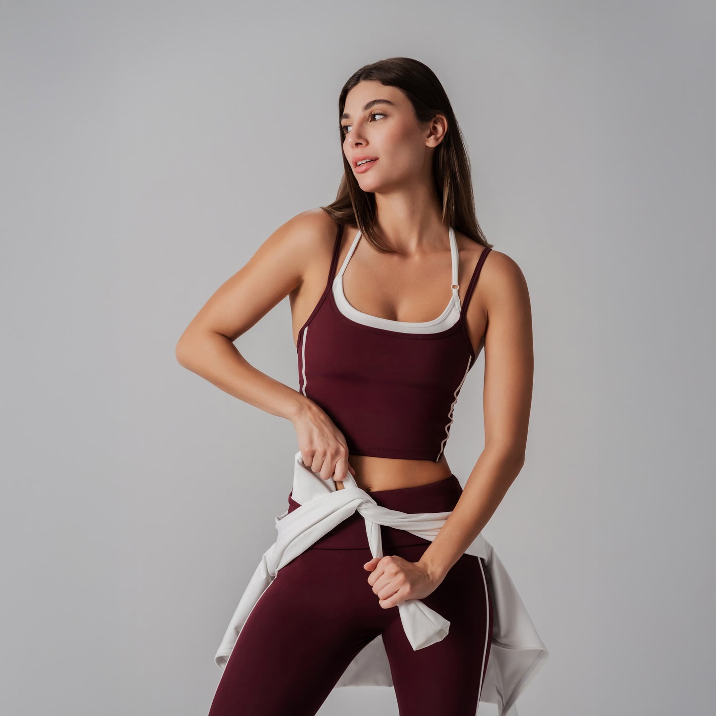 Woman in maroon athletic outfit holding a jacket against a plain background