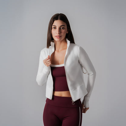 Woman wearing a white jacket over a maroon sports bra and leggings on a gray background
